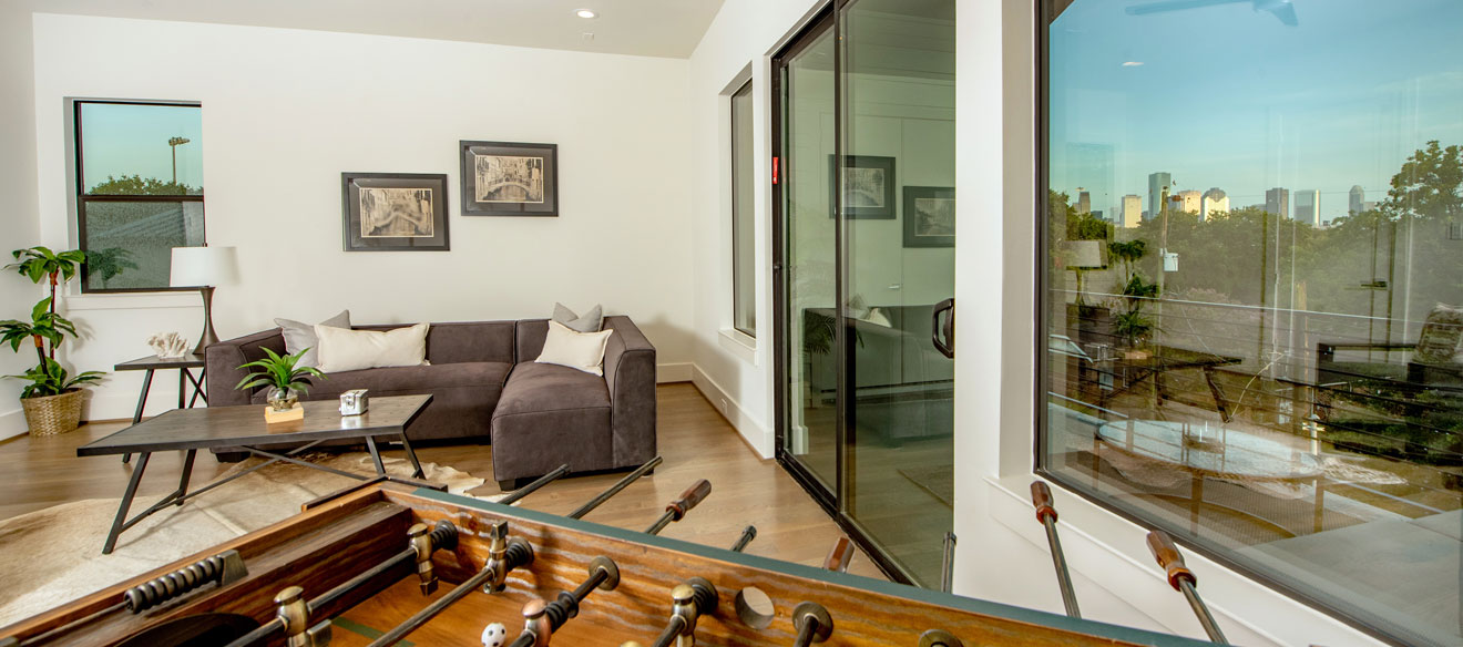 Covered patio area furnished with a sectional sofa and foosball table. Glass doors and windows reflect the Houston skyline. 