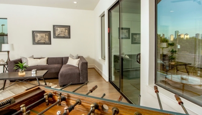 Covered patio area furnished with a sectional sofa and foosball table. Glass doors and windows reflect the Houston skyline. 