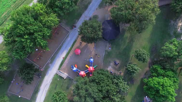 Aerial view of a children playing on the playground at Bellaire Park in Houston, Texas. Elevated view of slides, swings in the park surrounded by green trees.