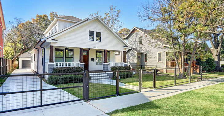 Bungalow style remodeled home, white exterior with dark wood porch, driveway leading to garage