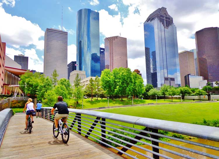 skyline view of Houston with two bicyclists riding over bike bridge