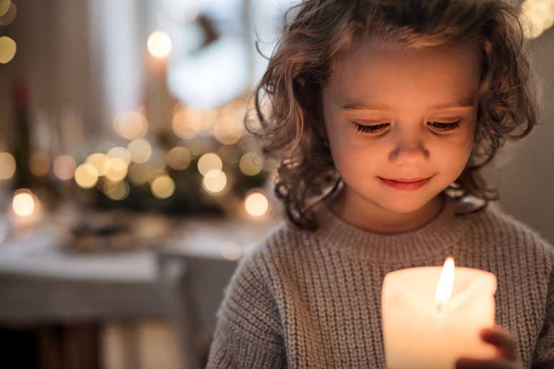 young girl looking a candle flame with decorative lights in the background