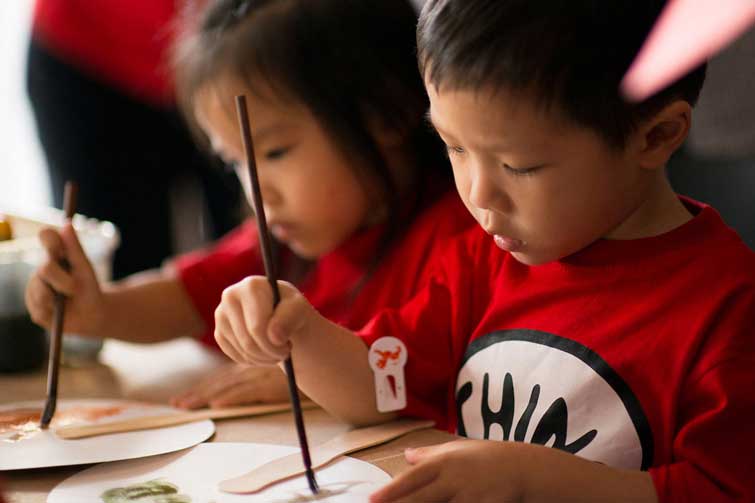Two young children with matching red shirts painting on paper plates