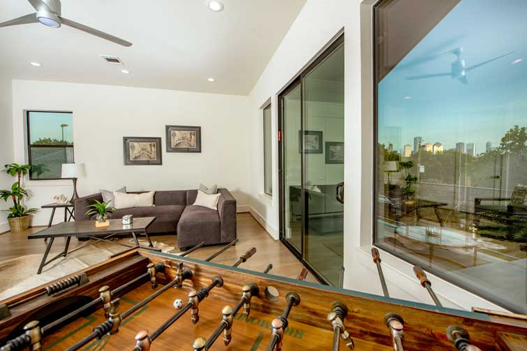 Living room with couches and foosball table connecting to balcony that overlooks downtown Houston